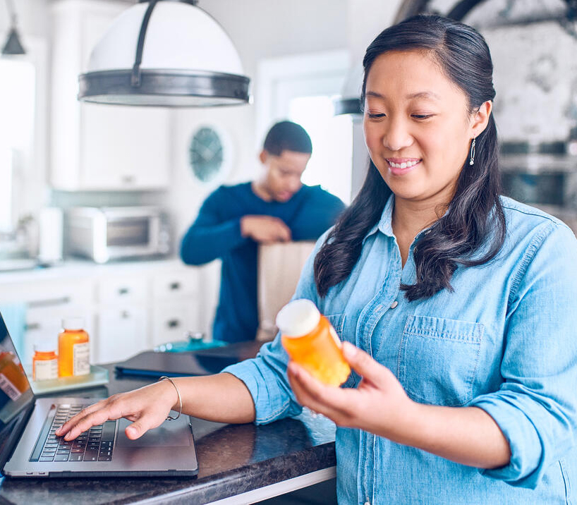 lady holding pill bottle on laptop