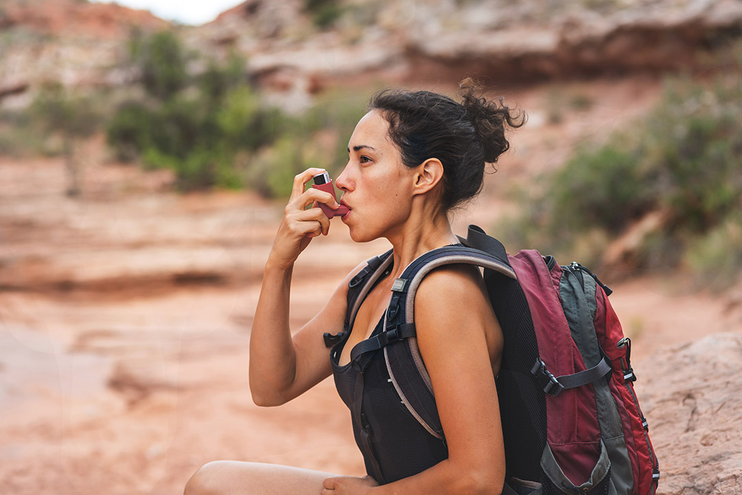 A young woman stops on a hike to use her rescue inhaler, which is an example of an as-needed medication.