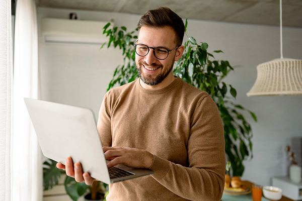 man in brown shirt and glasses smiling at laptop