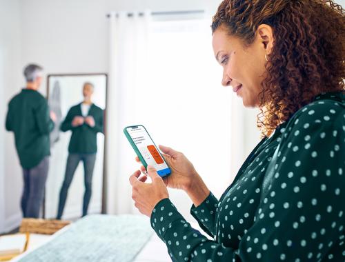 A woman sits on her bed while using her mobile device.